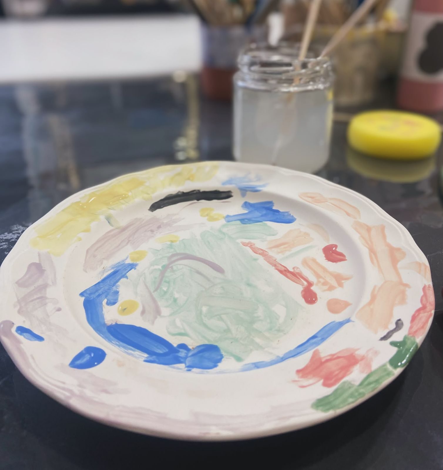 Plato pintado en un taller, con pinceles y botes de colores al fondo